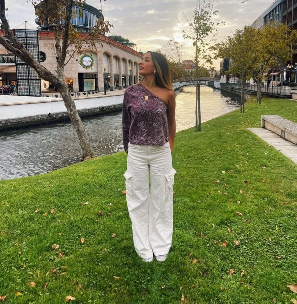 chica al lado de un canal con un oantalón cargo blanco y una blusa asimétrica con print blanco