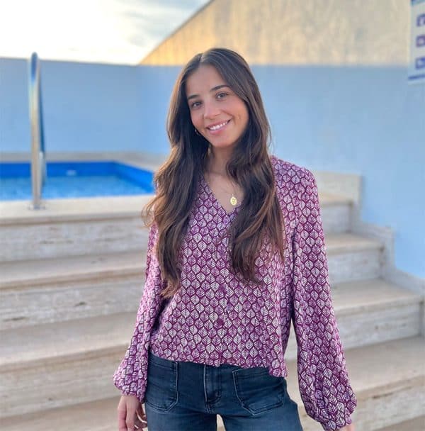 chica sonriendo con blusa burdeos con estampado de hojas pequeñas en color crudo y cuaro botones urdeos en el frontal, las mangas son abullonadas y con elastico en puños