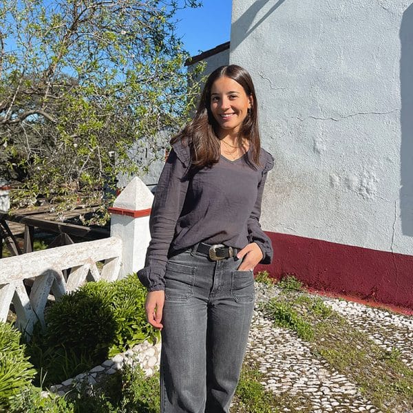 chica con las manos en los bolsillos de un pantalón tejano gris oscuro y blusa gris antracita con volantes en hombros