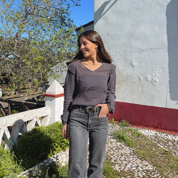 chica con las manos en los bolsillos de un pantalón tejano gris oscuro y blusa gris antracita con volantes en hombros