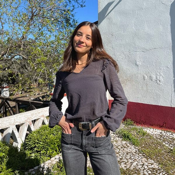 chica con las manos en los bolsillos de un pantalón tejano gris oscuro y blusa gris antracita con volantes en hombros