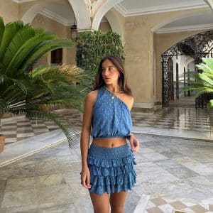 chica en un patio sevillano con un conjunto de top asimétrico azul con detalles plateados y falda pantalón con 4 volantitos y cintura fruncida