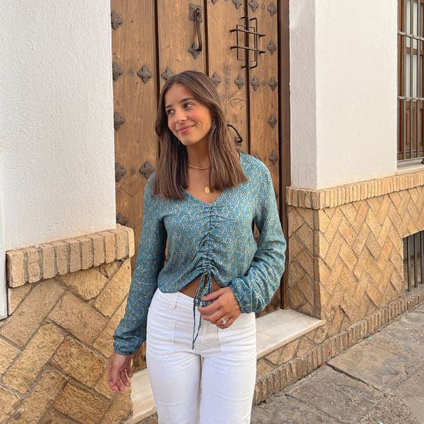 chica sonriendo con la mano en el pantalón blanco con una blusa fruncida en frontal con cordón de manga larga en verde con print amarillo