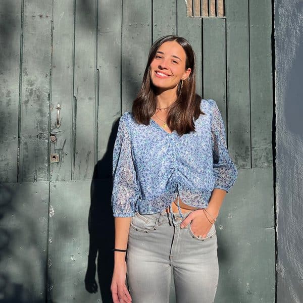 chica delante de una puerta de madera verde con una blusa de gasa de manga francesa y cordón frontal para fruncir en estampado azul con lúrex