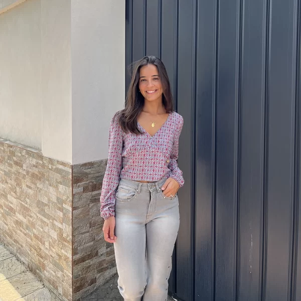 chica en la calle delante de una puerta de garaje gris con blusa modelo Cádiz con estampado verde agua y coral y pantalón gris con tachuelas plateadas