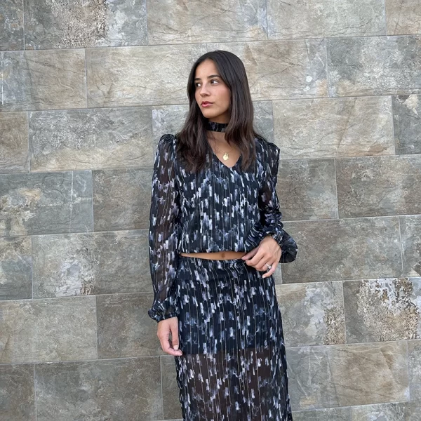 chica sonriendo delante de una pared con una blusa de gasa negra estampada blanco y celeste con choker en cuello del mismo tejido y una falda larga de gasa del mismo tejido y print que la blusa