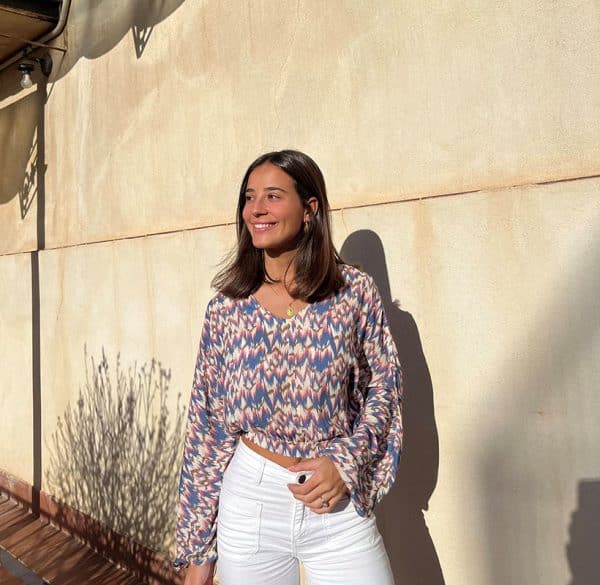 chica sonriendo con una blusa de hombros descubiertos, corta en tonos celestes y rosas