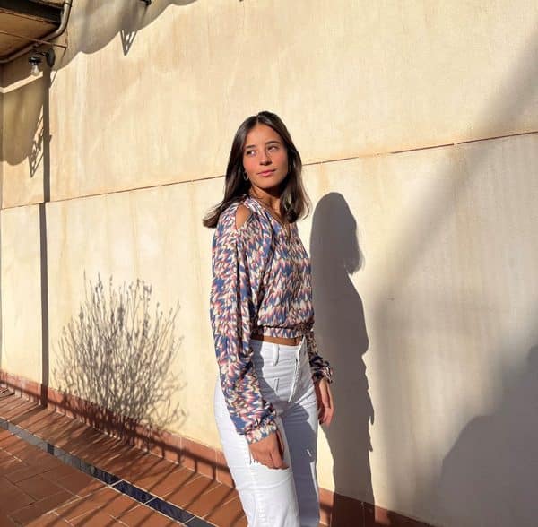 chica sonriendo con una blusa de hombros descubiertos, corta en tonos celestes y rosas