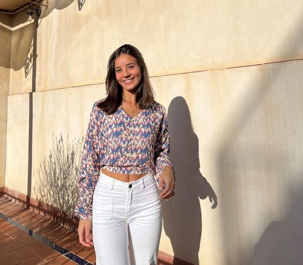 chica sonriendo con una blusa de hombros descubiertos, corta en tonos celestes y rosas