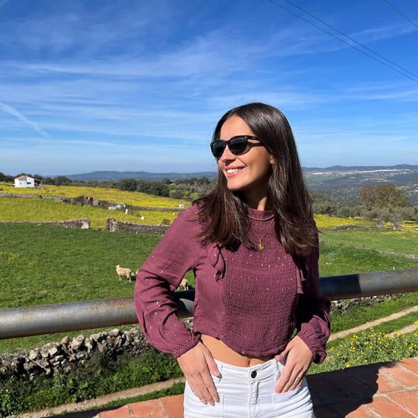 chica en el campo con gafas de sol con pantalón blanco y blusa fruncida en frontal y trasero de manga larga con volantes en hombros y lúrex plata