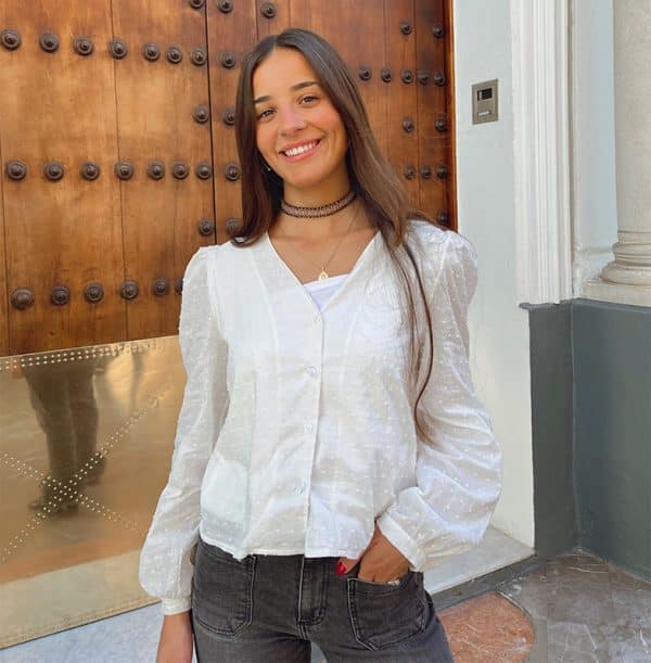 chica sonriendo con blusa de manga larga y escote pico sin cuello de plumeti blanca