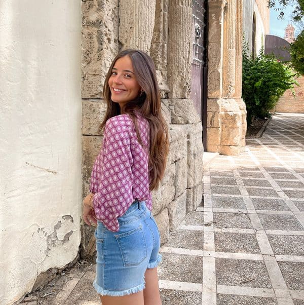 chica sonriendo con short denim azul desflecado en bajo y blusa