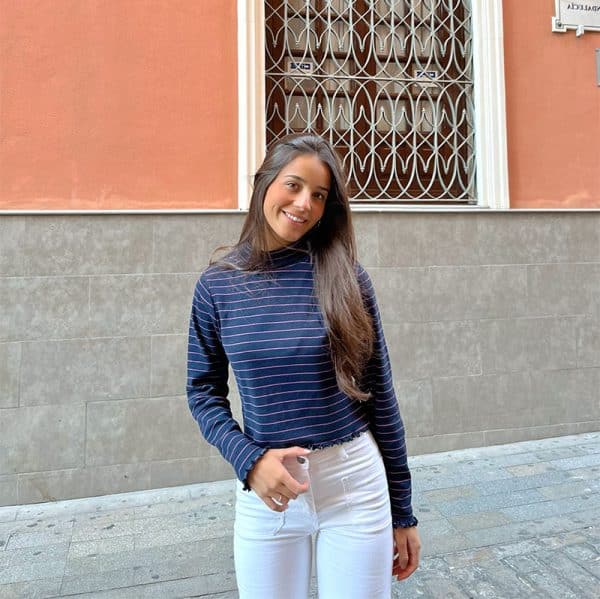 chica sonriendo con mano en el bolsillo con camiseta de cuello vuelto en color marino y rayas finas rosas