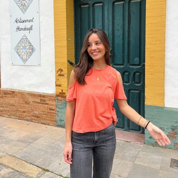 chica con una camiseta naranja con hombros descubiertos y tejano gris