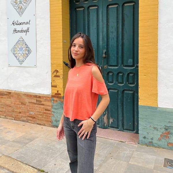 chica con una camiseta naranja con hombros descubiertos y tejano gris