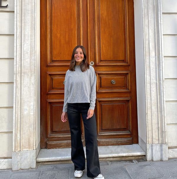 chica sonriendo con una camiseta oversize gris con rayas negras y pantalón campana negro