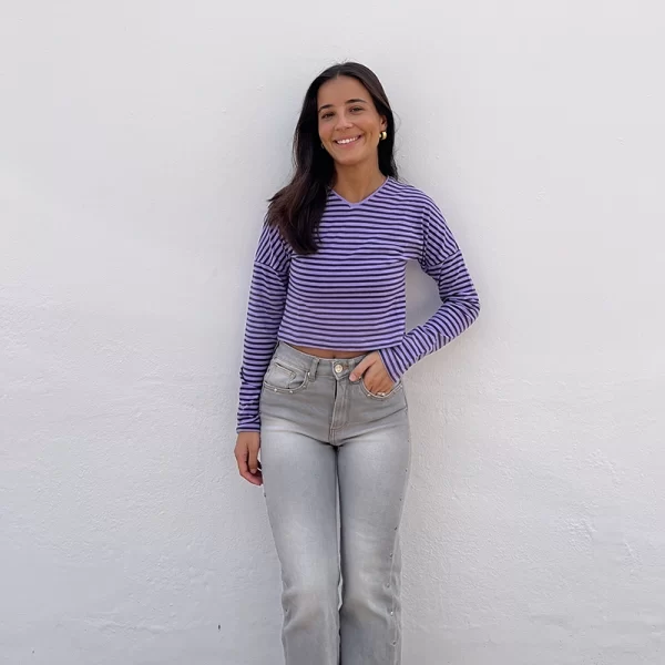 chica apoyada en una pared blanca con una camiseta corta de cuello pico de rayas antracita y lila