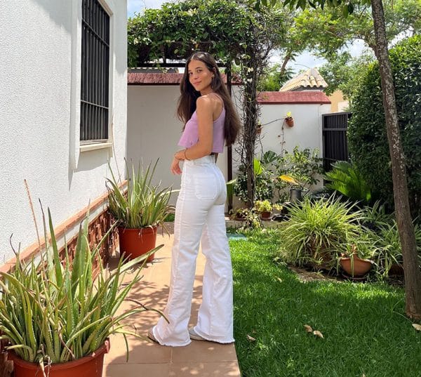 chica en un jardin con pantalon campana blanco y top crop malva