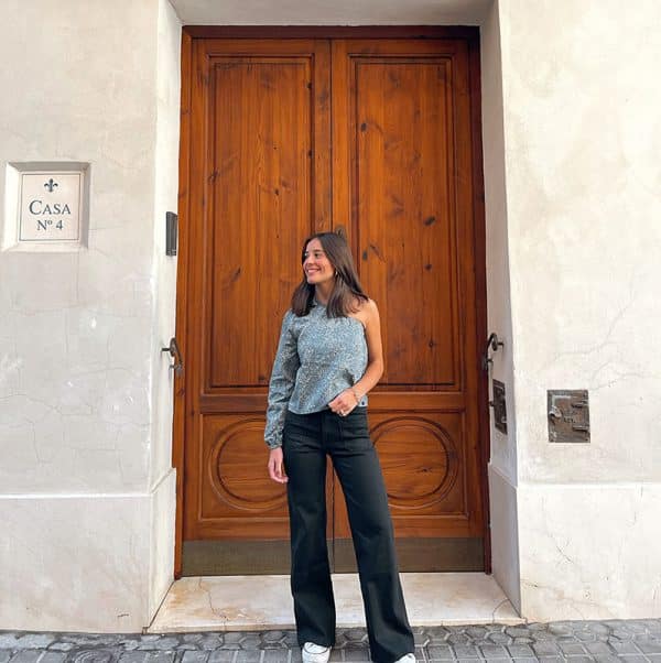 chica sonriendo con una blusa asimétrica verde con print crudo y pantalón campana negro