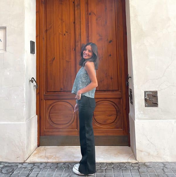 chica sonriendo con una blusa asimétrica verde con print crudo y pantalón campana negro