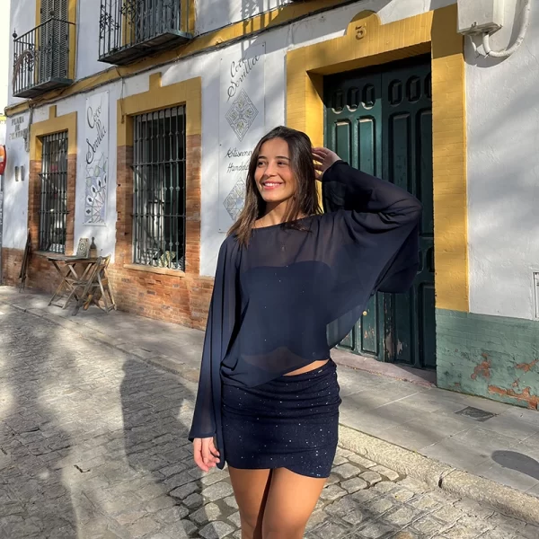 chica sonriendo delante de una puerta de madera verde con un conjunto azul de brillo de falda corta y top banda y una capa de gasa azul