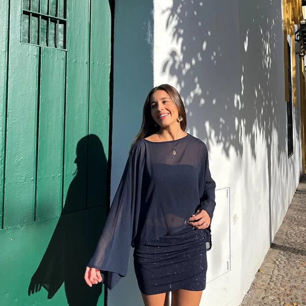 chica sonriendo delante de una puerta de madera verde con un conjunto azul de brillo de falda corta y top banda y una capa de gasa azul