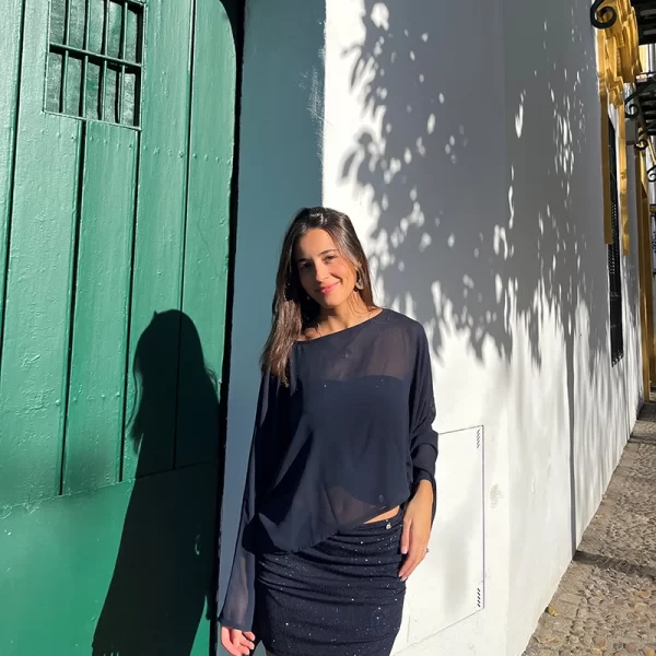 chica sonriendo delante de una puerta de madera verde con un conjunto azul de brillo de falda corta y top banda y una capa de gasa azul