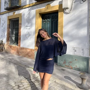 chica sonriendo delante de una puerta de madera verde con un conjunto azul de brillo de falda corta y top banda y una capa de gasa azul