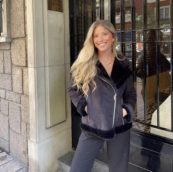 chica sonriendo en la calle con las manos en los bolsillos de una chaqueta negra de doble faz