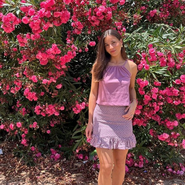 chica delante de una pared de flores fucsias con un top anudado al cuello rosa viejo y falda de gomas elástica fruncida con volante en bajo estampada rosa viejo con blanco