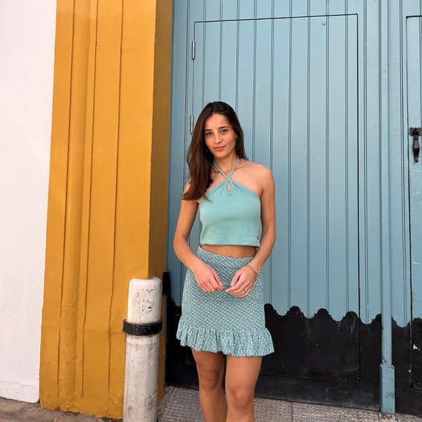 chica delante de un portón verde agua vestida con un conjunto de top banda cuello halter en verde wasabi y falda estampada verde