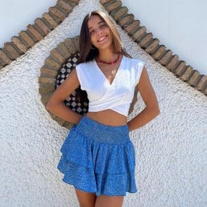 chica sonriendo con un top blanco cruzado y una falda pantalon corta con dos volantes y ciintura fruncida de color azul