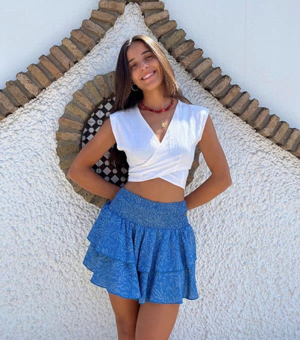 chica sonriendo con un top blanco cruzado y una falda pantalon corta con dos volantes y ciintura fruncida de color azul