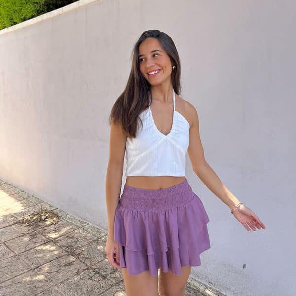 chica morena con un top blanco con líneas de hilo de lúrex plateado y una falda pantalón rosa viejo con cintura fruncida y dos volantes