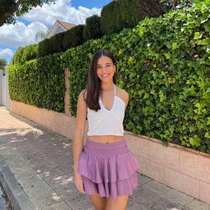 chica morena con un top blanco con líneas de hilo de lúrex plateado y una falda pantalón rosa viejo con cintura fruncida y dos volantes