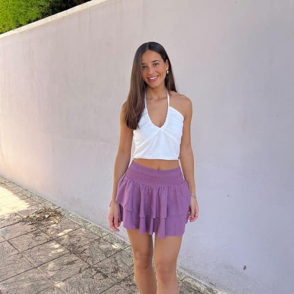 chica morena con un top blanco con líneas de hilo de lúrex plateado y una falda pantalón rosa viejo con cintura fruncida y dos volantes