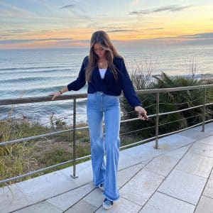 chica delante del mar con una blusa azul marino cruzada y un pantalón tejano azul desflecado en bajo