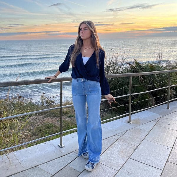 chica delante del mar con una blusa azul marino cruzada y un pantalón tejano azul desflecado en bajo