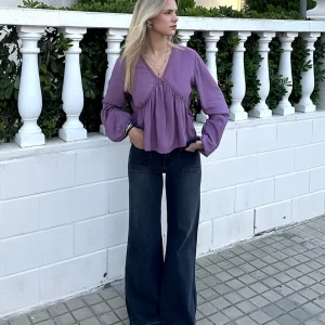 chica posando en la calle con un pantalón campana gris oscuro con dos bolsillos frontales y blusa rosa de escote pico con intersecciones con cuello