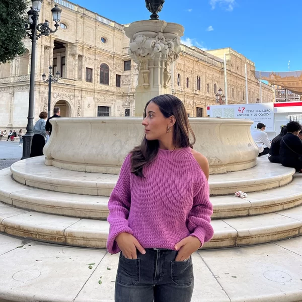 chica posando en la calle con un jersey rosa con el hombro izquierdo descubierto