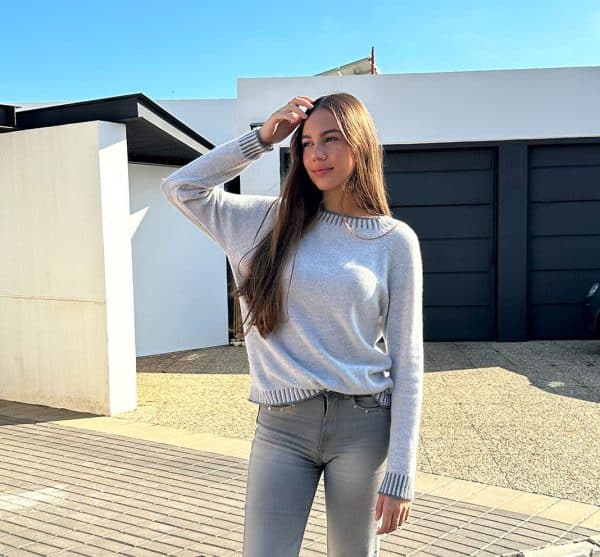 chica delante de una puerta gris antracita con un jersey gris de cachemir con pespuntes a sobre tono en cuello, puño y bajo