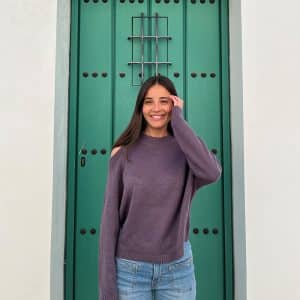 chica delante de una puerta verde con un jersey morado de hombros descubiertos y pantalón campana azul con tachuelas en frontal y lateral