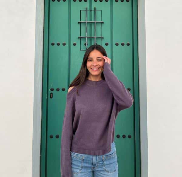 chica delante de una puerta verde con un jersey morado de hombros descubiertos y pantalón campana azul con tachuelas en frontal y lateral