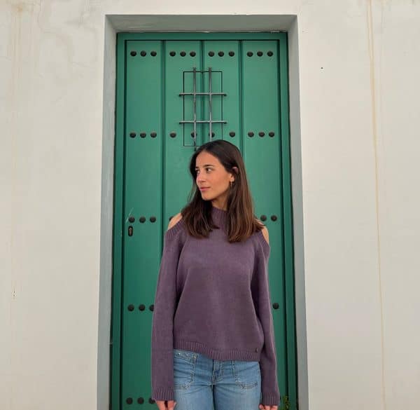 chica delante de una puerta verde con un jersey morado de hombros descubiertos y pantalón campana azul con tachuelas en frontal y lateral