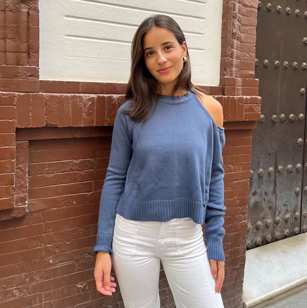 chica posando con un jersey azul con el hombro izquierdo descubierto y pantalón blanco