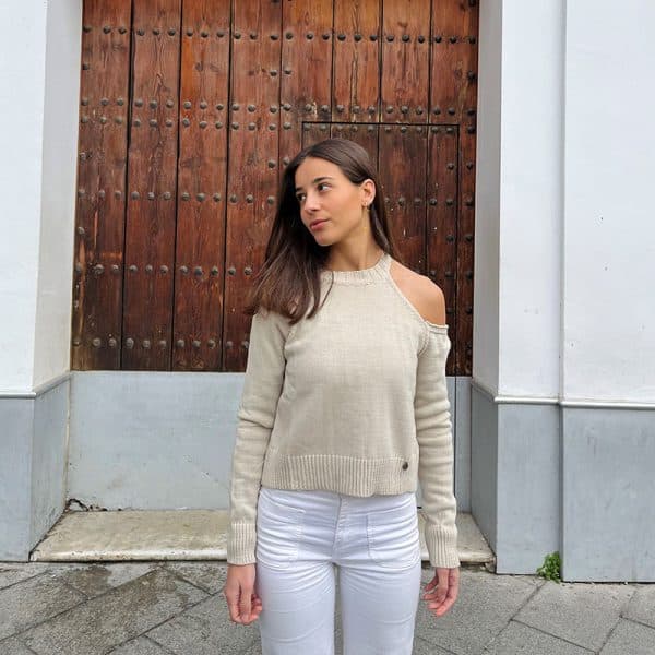 chica delante de una puerta de madera con un jersey con hombro izquierdo descubierto en color beige