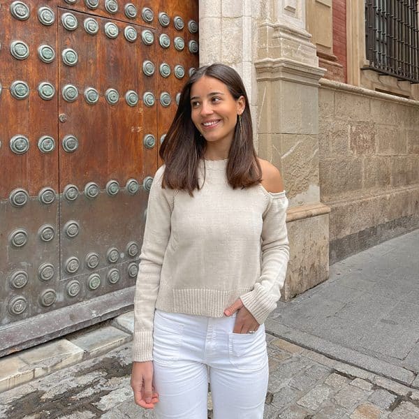 chica delante de una puerta de madera con un jersey con hombro izquierdo descubierto en color beige