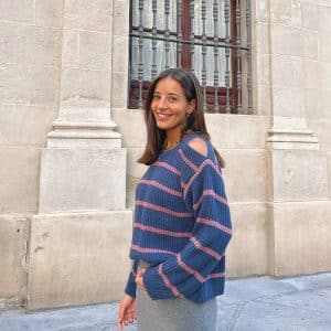 chica de perfil sonriendo con un jersey azul de rayas rosas con hombros descubiertos