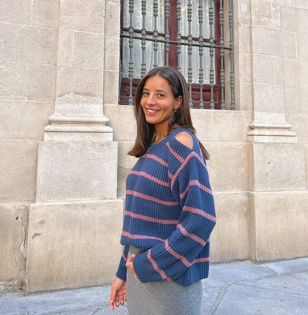 chica de perfil sonriendo con un jersey azul de rayas rosas con hombros descubiertos