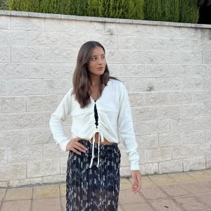 chica delante de una pared blanca con un jersey chaqueta beige abierto en frontal y cerrado con cordón con falda de gasa estampada negra